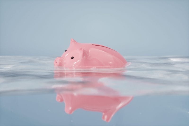 pink piggy bank sinking into water meant to symbolize the value of money sinking